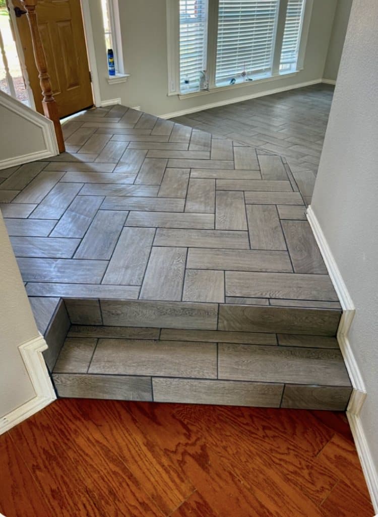 Wood-look porcelain tile set in a herringbone pattern across an entry and steps